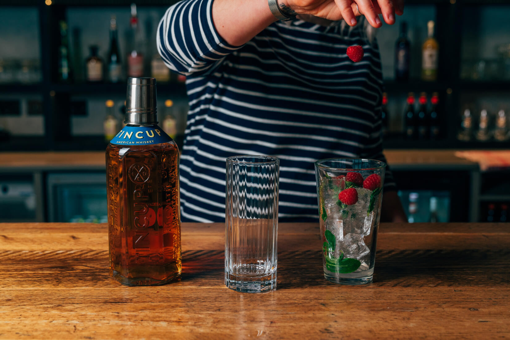 Lady prepping whiskey side mule cocktail with tall glass and ice