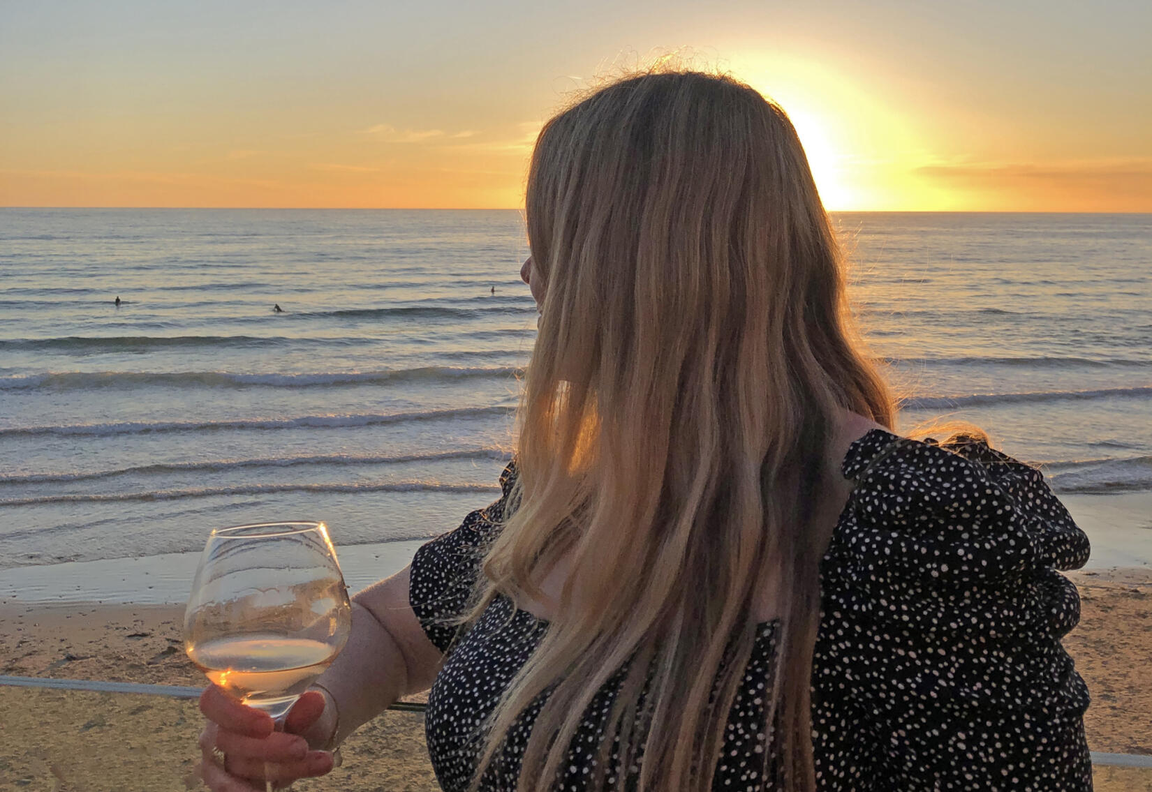 Anna Jones holds a glass of wine and looks out across the sea to the sunset