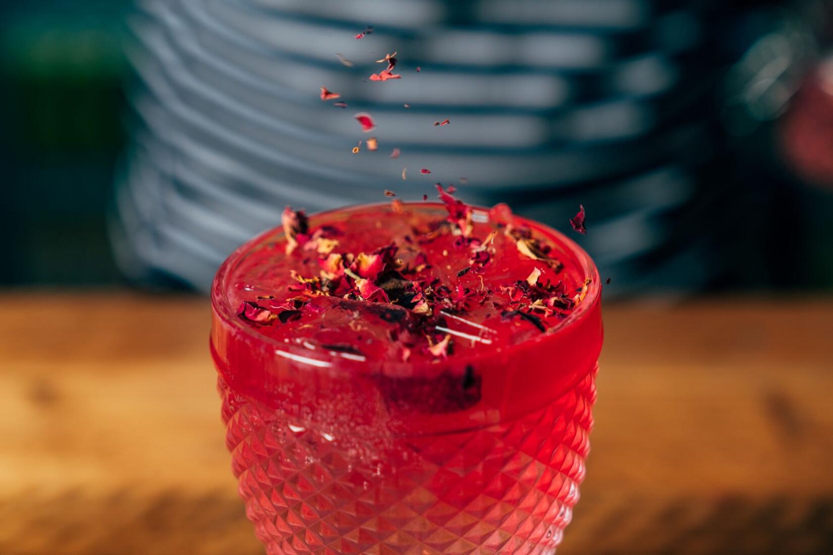 Blueberry and rose collins cocktail in a short glass with petals dusted on top