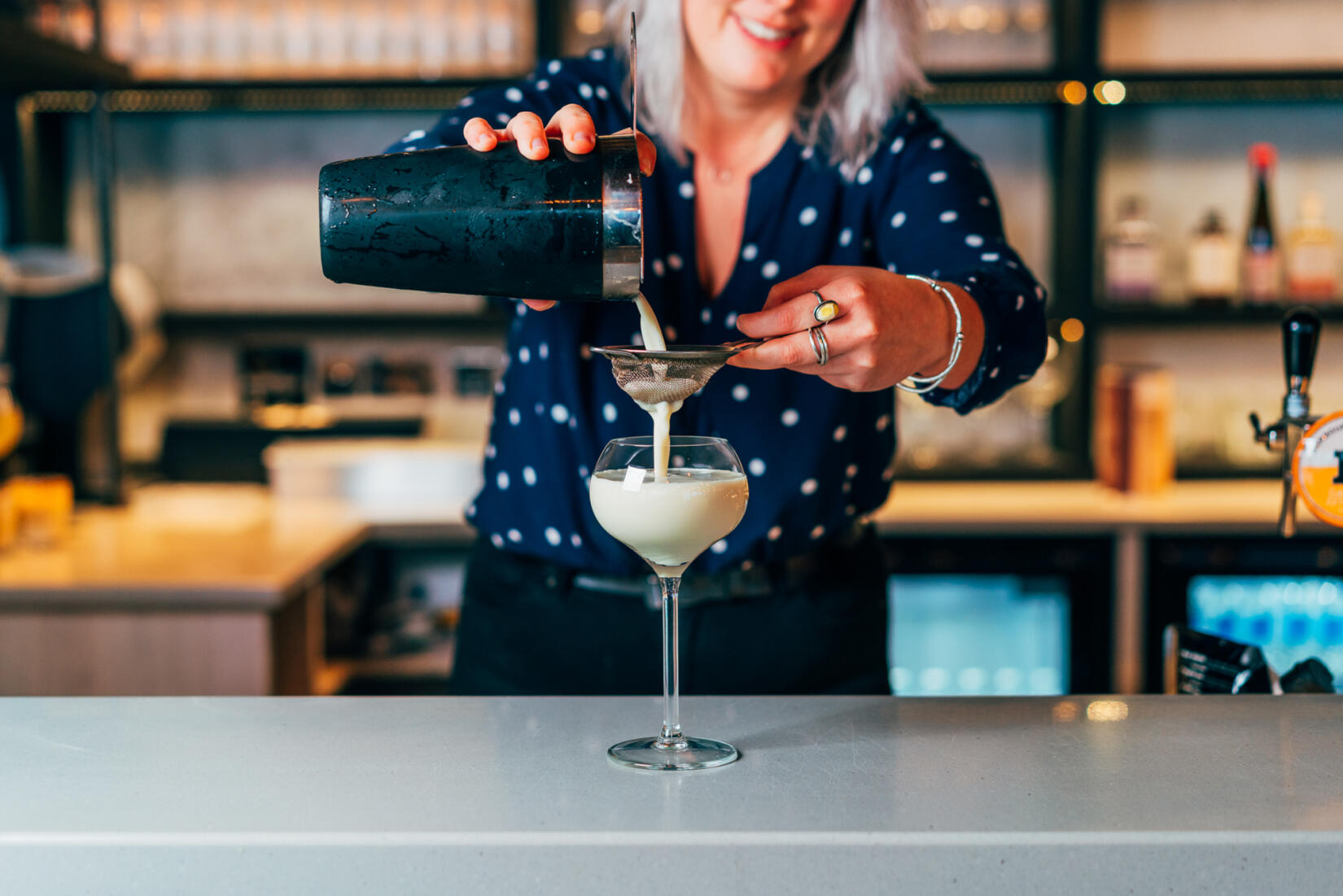 Lady pouring winter colada cocktail into large glass with sieve