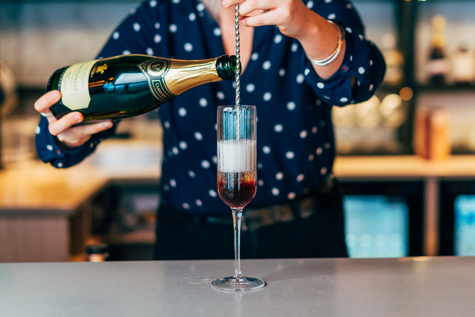 Bar tender pouring champagne into kir royale cocktail glass