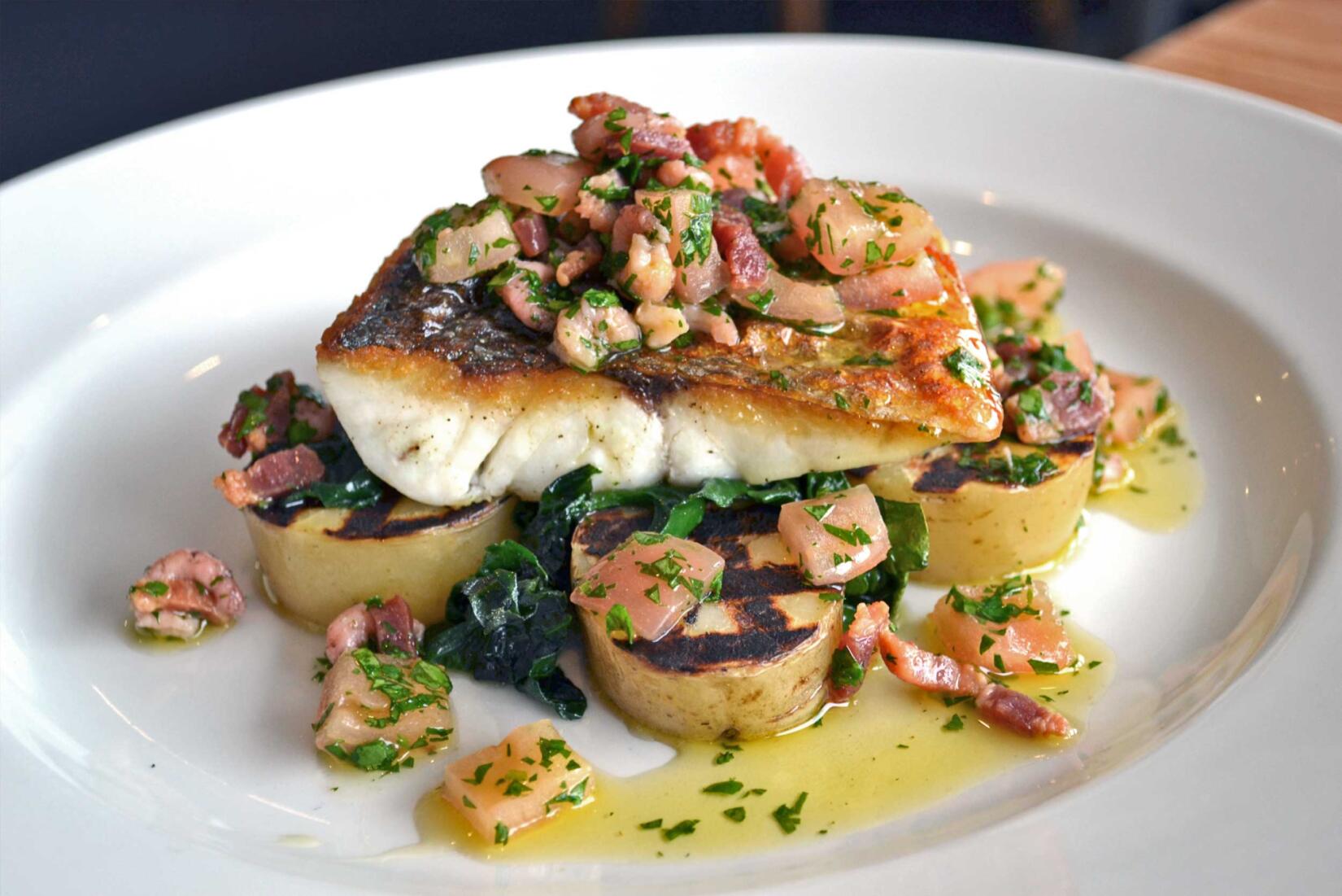 A plate of wild sea bass, potatoes, spinach and tomato