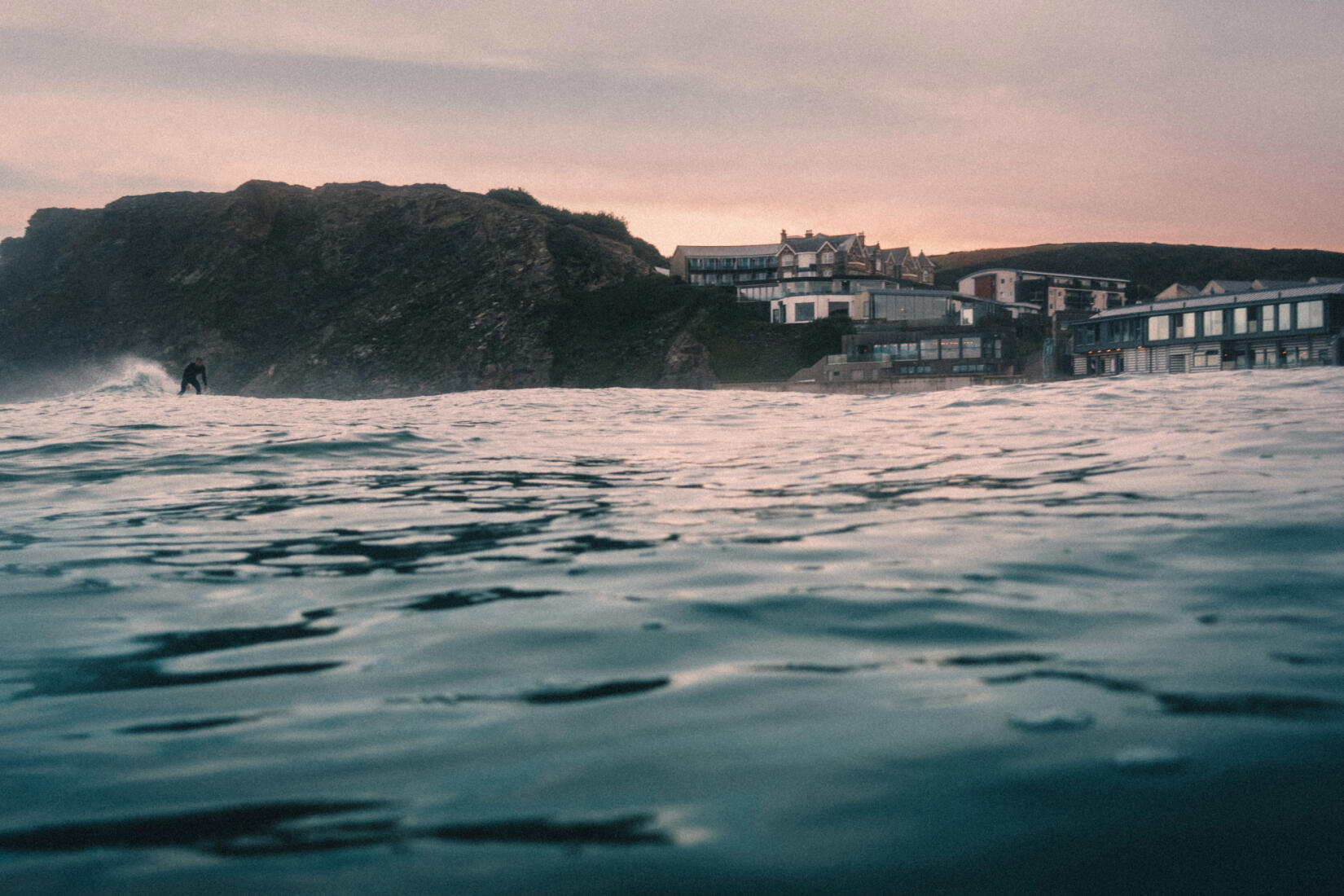 Watergate Bay hotel from the sea at dusk with a surfer in shot