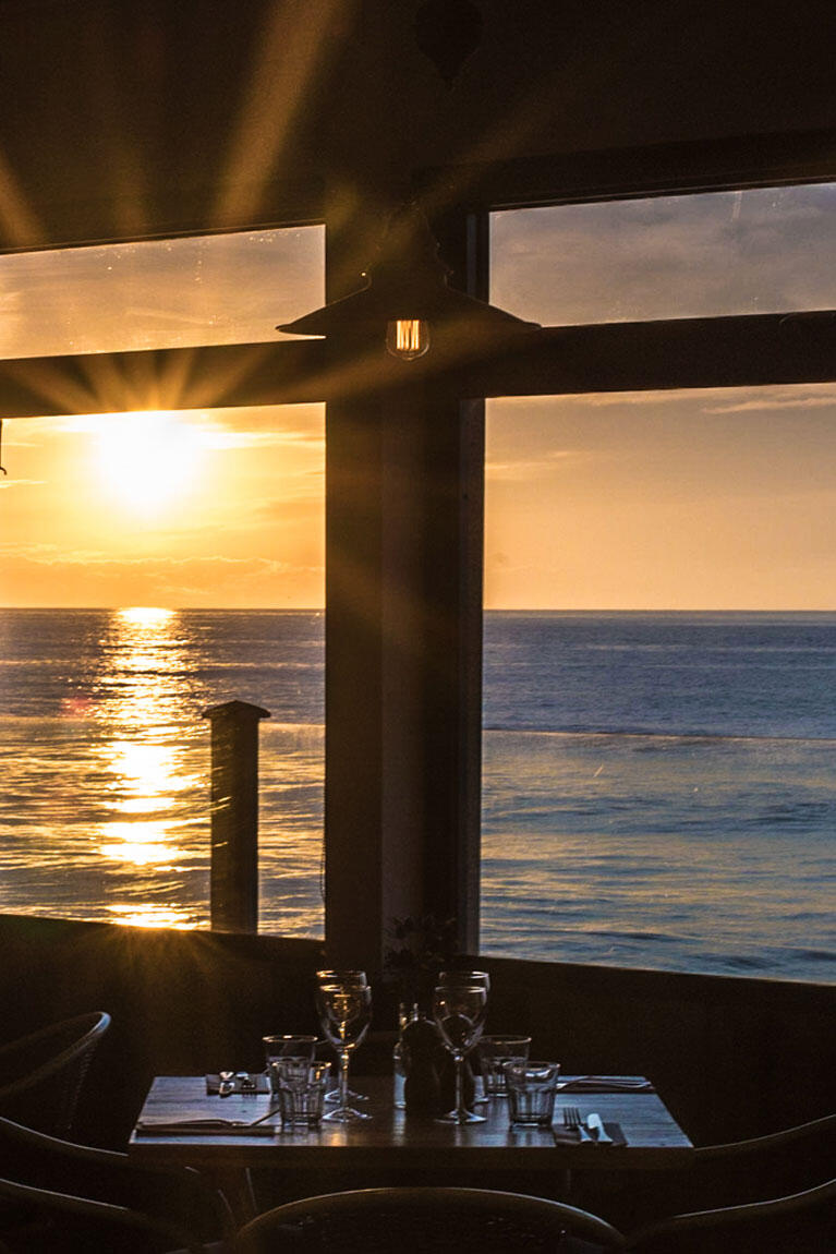 Restaurant table laid up ready for guests in front of the sea view sunset at Watergate Bay
