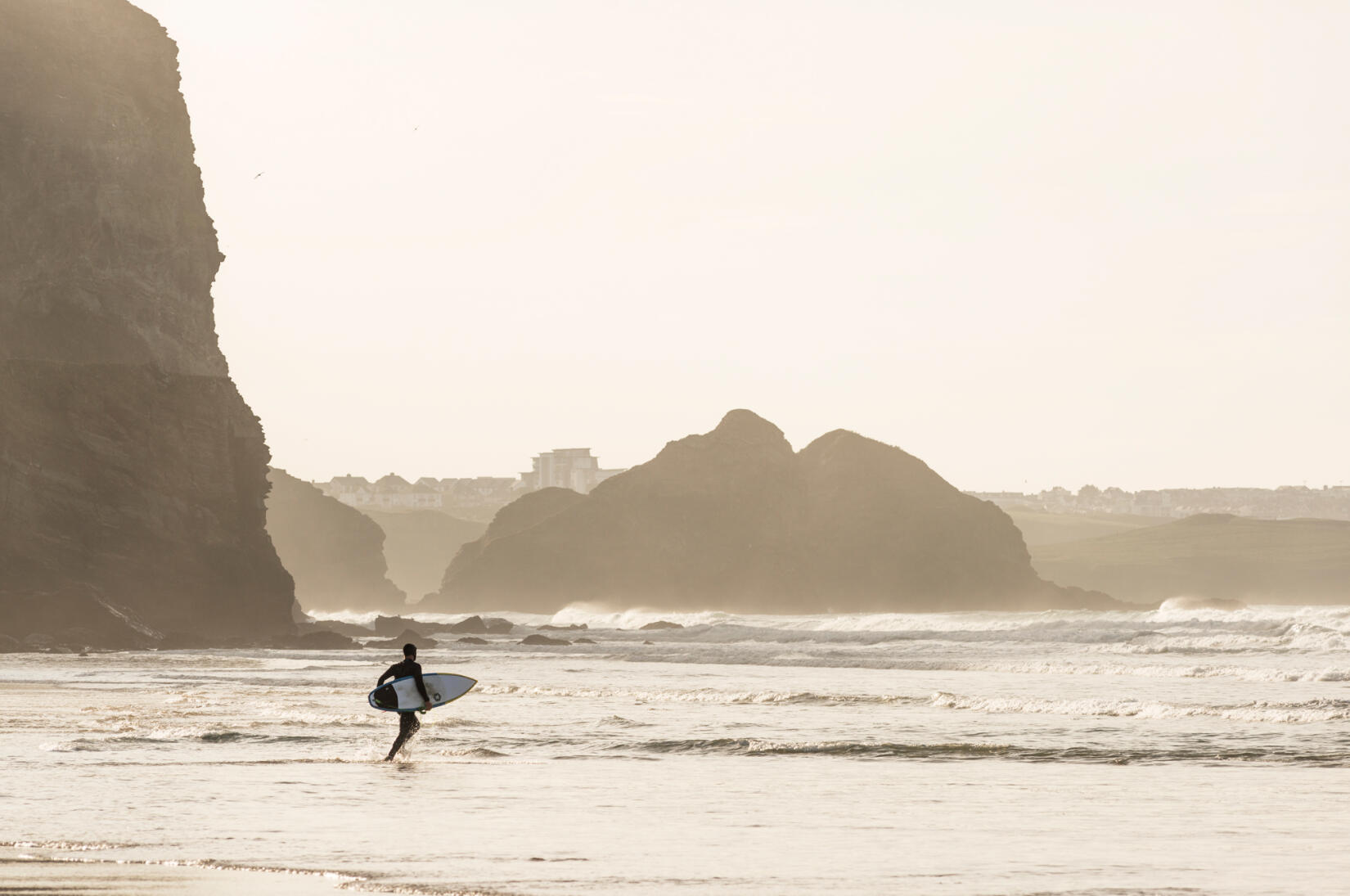 A surfer walks out into the break with a board under their arm