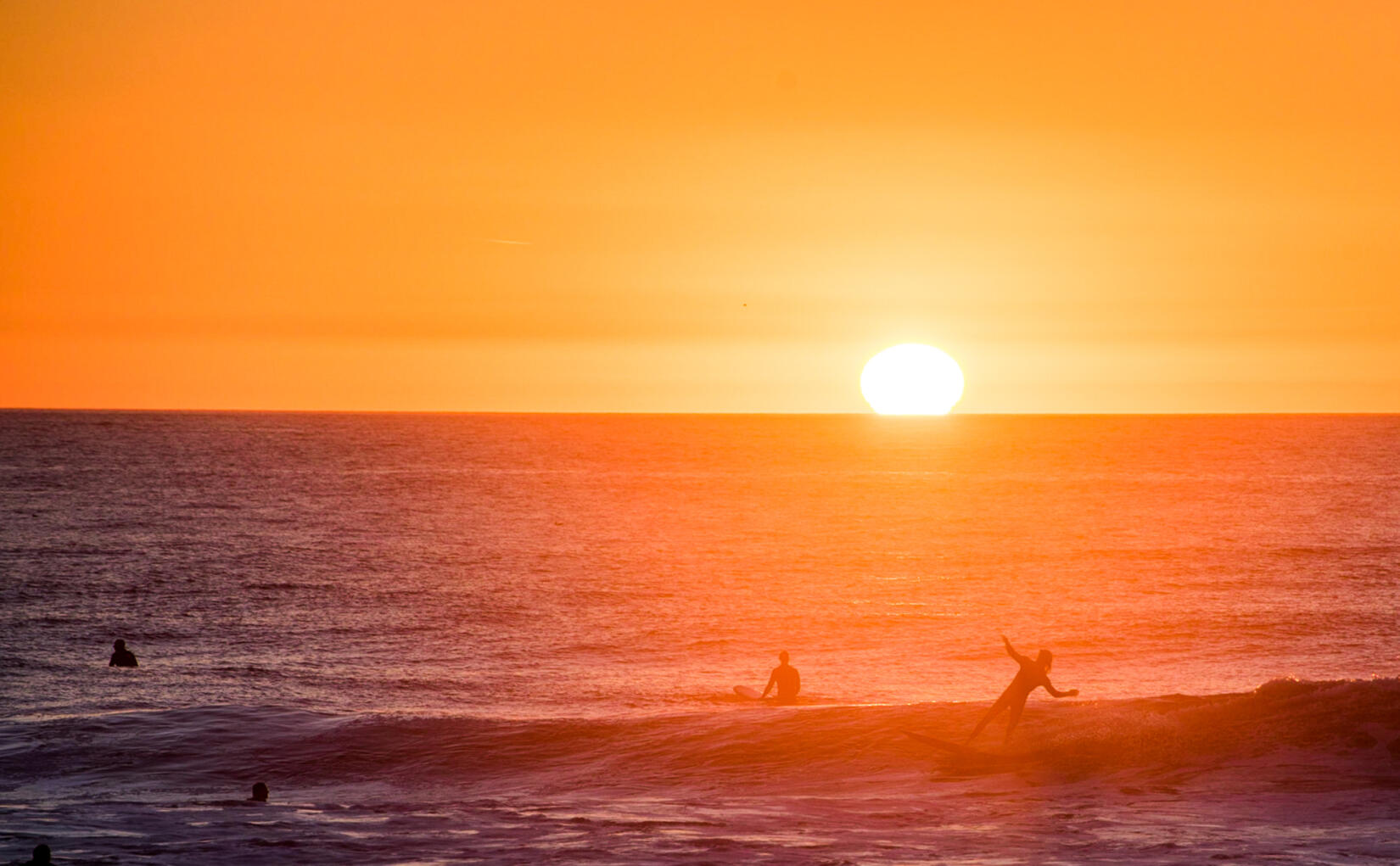 Surfer pulls off a wave with a golden sunset behind