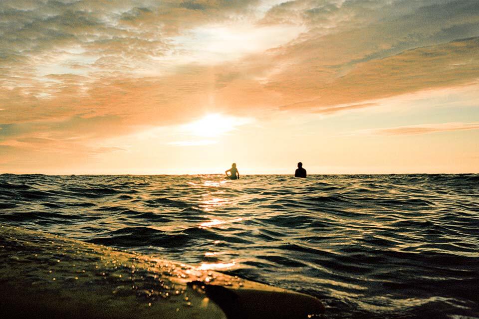 Two surfers in the sunset out at sea