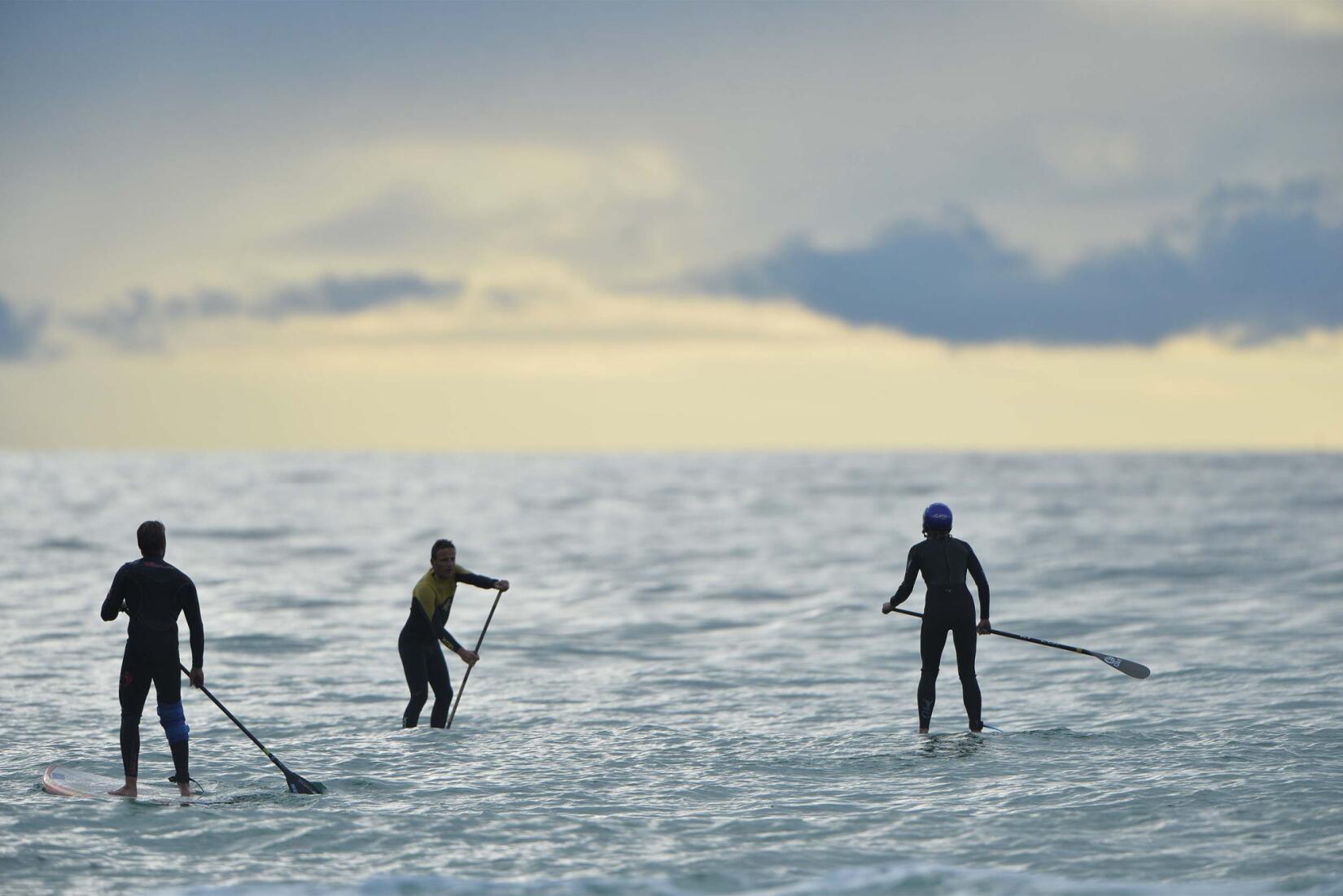 Three standup paddleboarders on the water at Watergate Bay