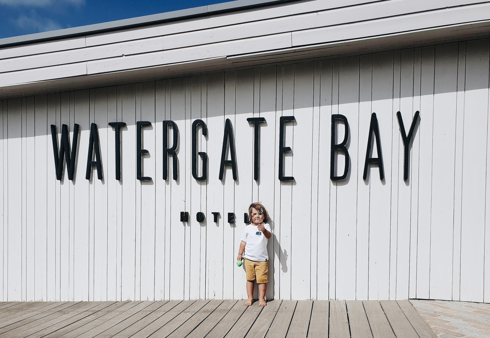 Young boy holding a windmill stood in front of Watergate Bay Hotel sign