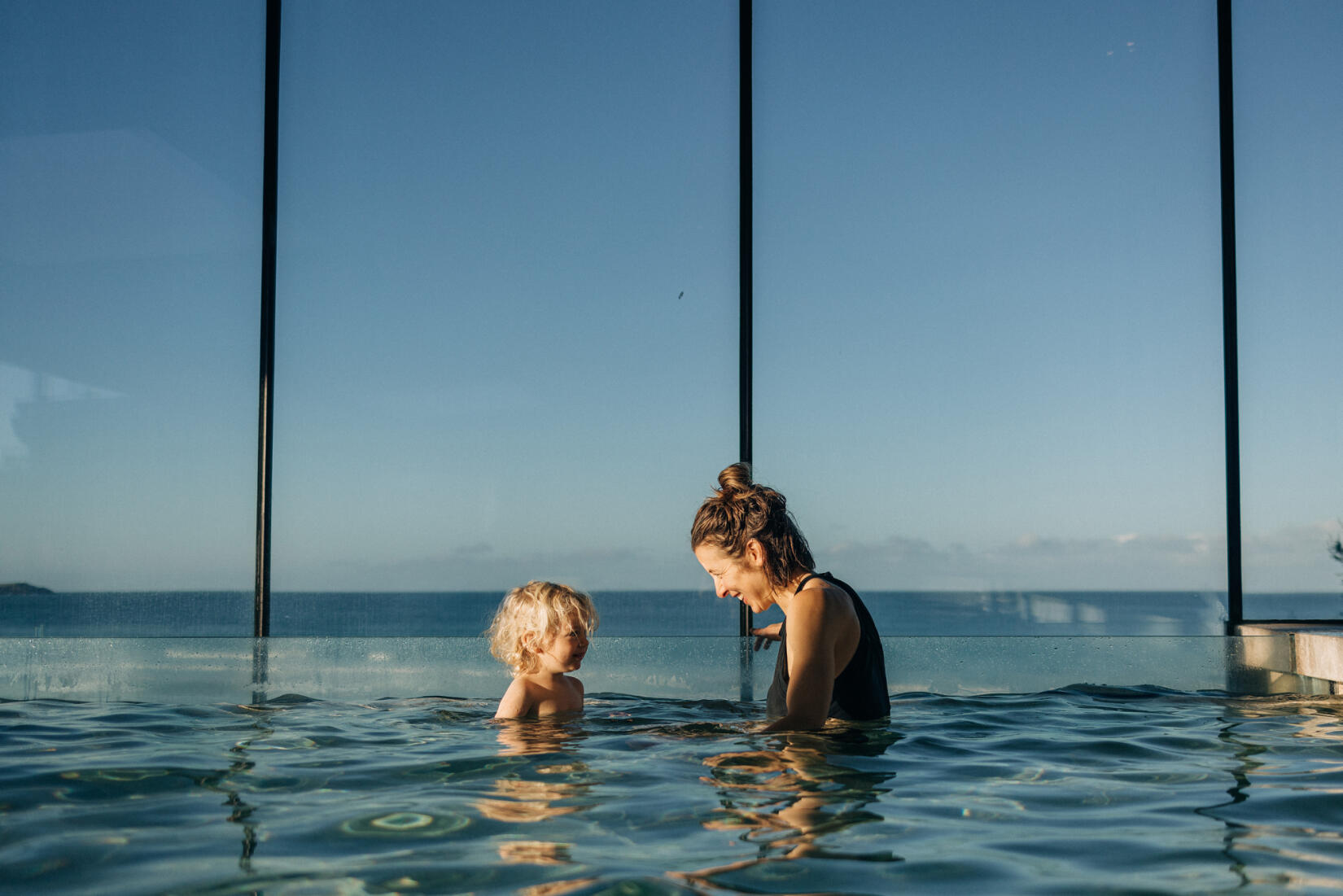 Mother and toddler enjoying the infinity pool with the sea view behind them