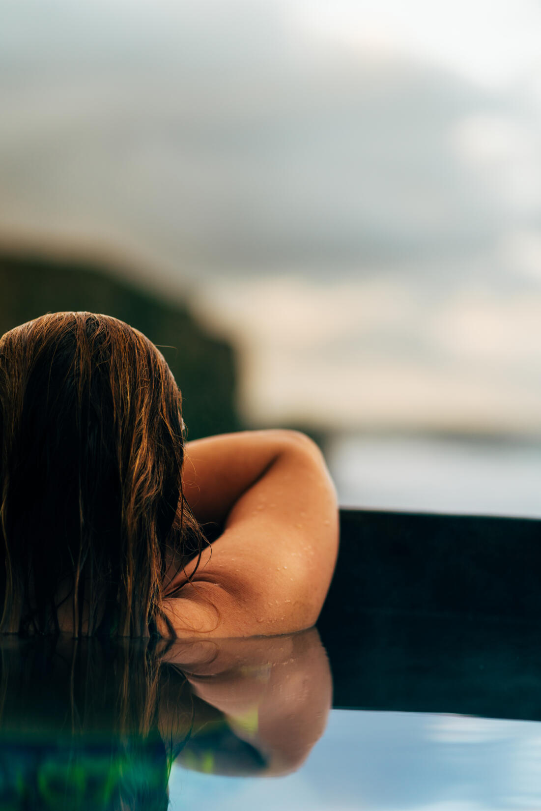 A woman sitting in the hot tub on the deck of Swim Club overlooking the beach at Watergate Bay