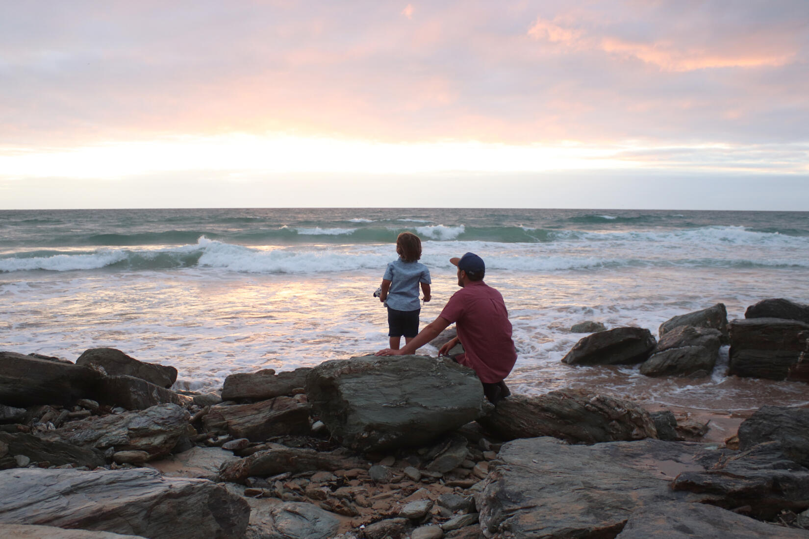 Father and son watching the waves from the rocks at dusk