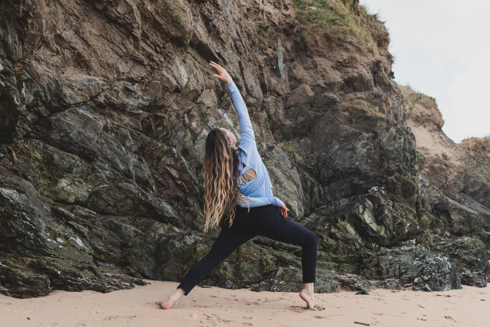 A lady doing yoga on the sand in front of large cliffs