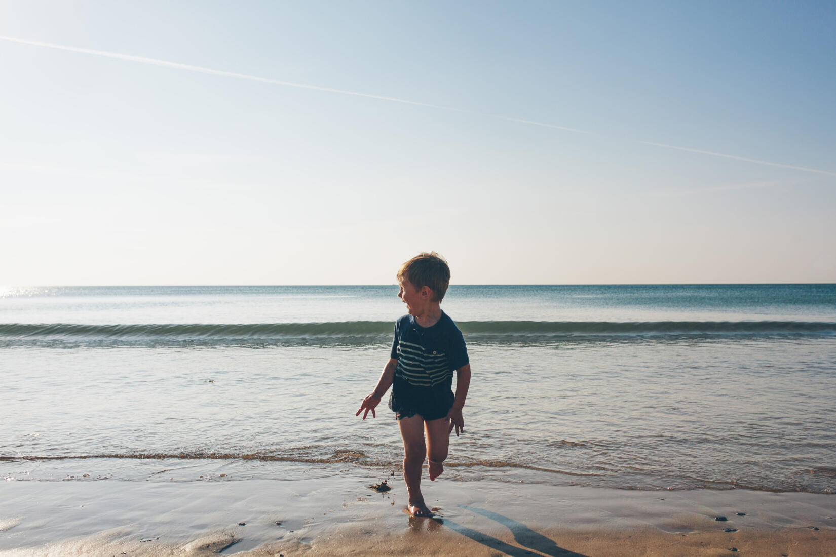 A young boy runs on the sand as the waves chase him in