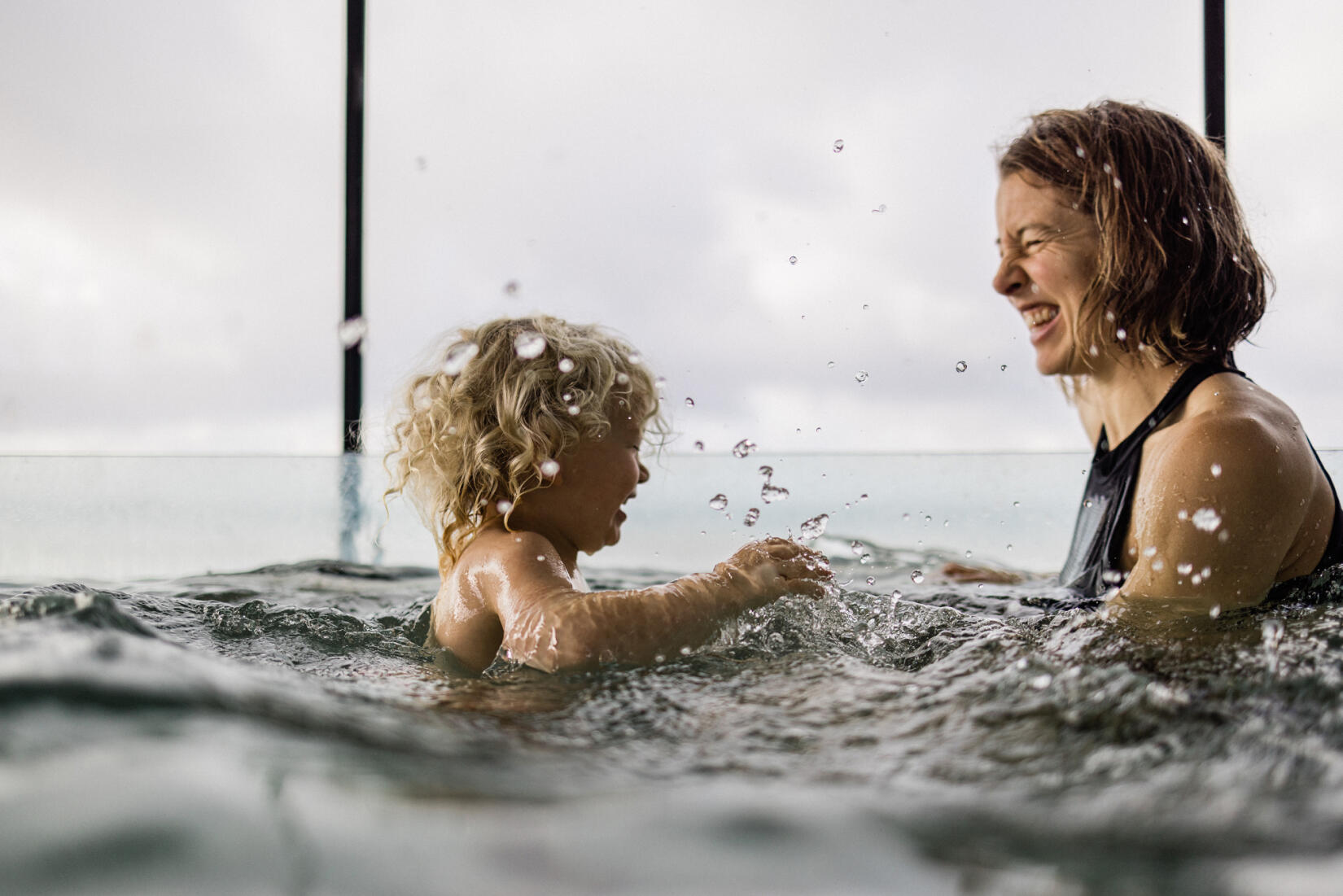 Mother and toddler laughing, splashing in the swimming pool