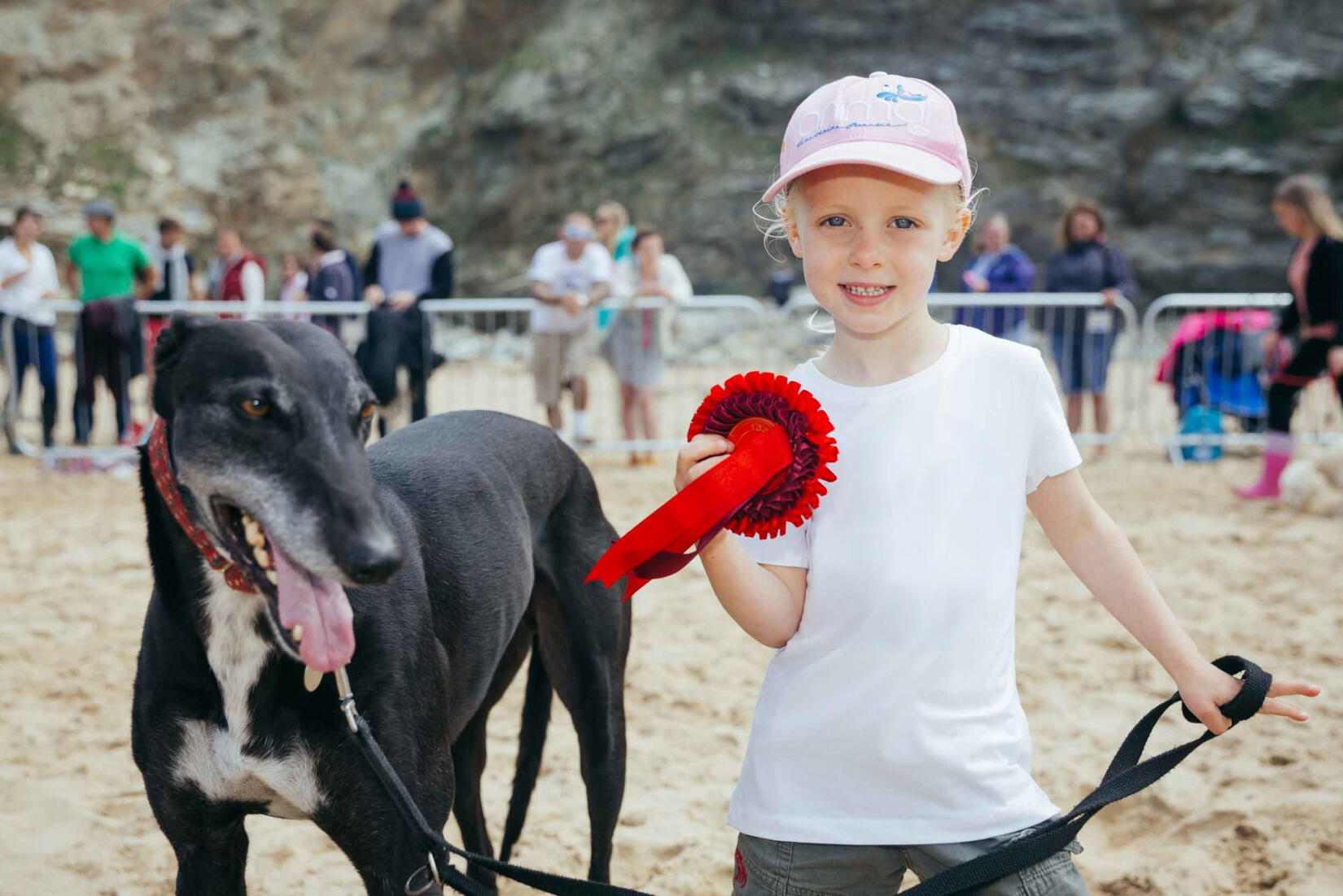 Little girl with her winning dog and red rosette on the beach at Watergate Bay