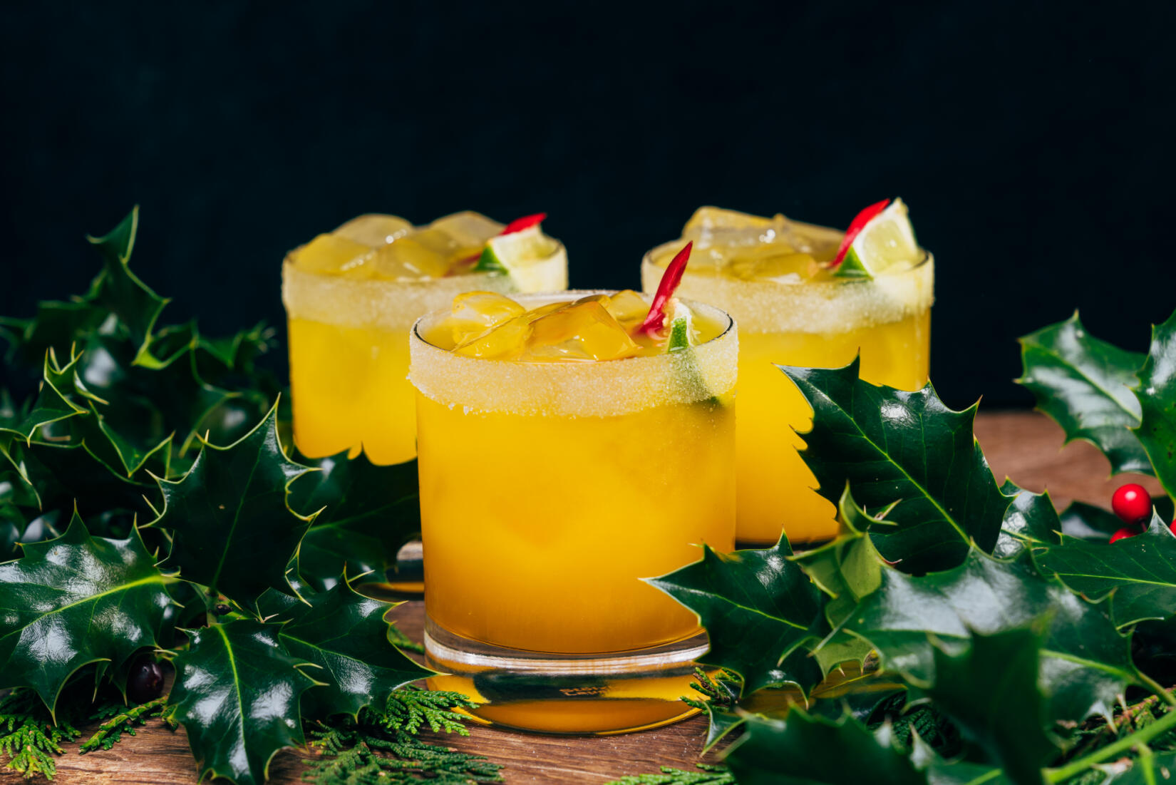 Glasses of Spicy Clementine Margarita cocktail with holly in the foreground