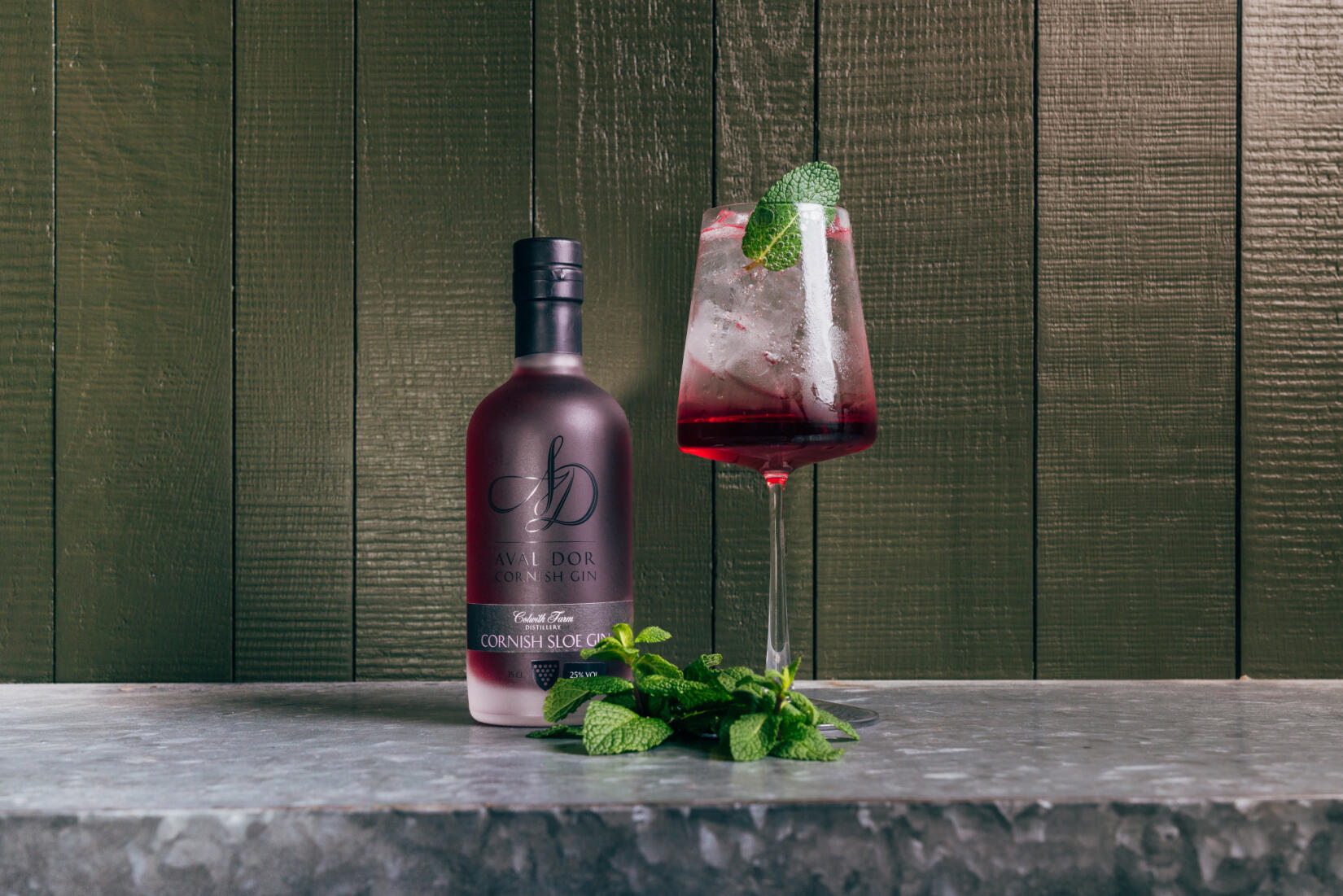 Cocktail in a wine glass with a bottle of sloe gin