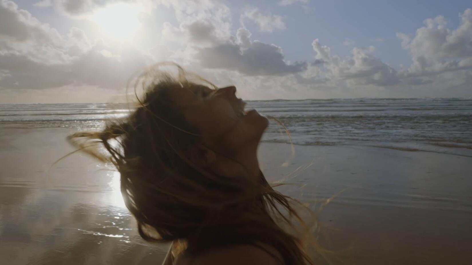 Close up of a woman looking uo to the sky and laughing as she runs on the shoreline