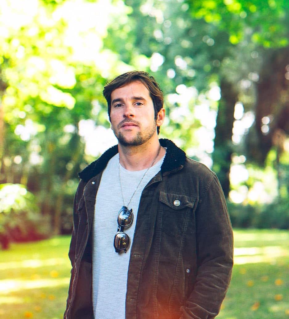 An image of musician Joe Hurworth standing with a woodland behind him