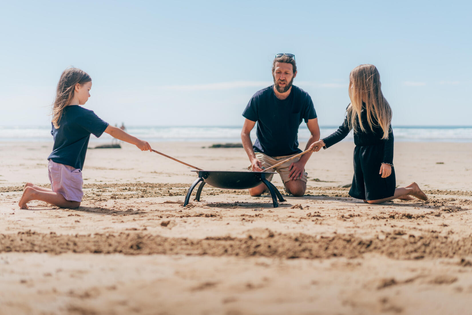 two children toasting marshmallows on the beach with beach school team member around a fire