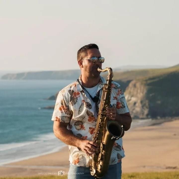A photo of a saxophonist playing with the backdrop of a beach and cliffs