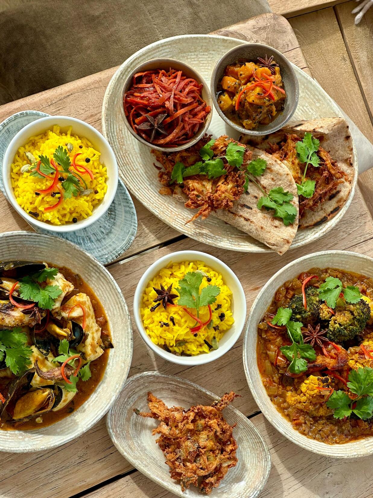 Top down photograph of a range of colourful curry dishes and sides at The Beach Hut